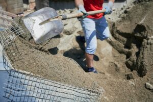 Male worker shoveling sand-cement mix at construction site.